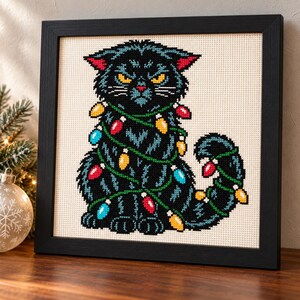 Christmas lights cat cross stitch in a black frame on a shelf