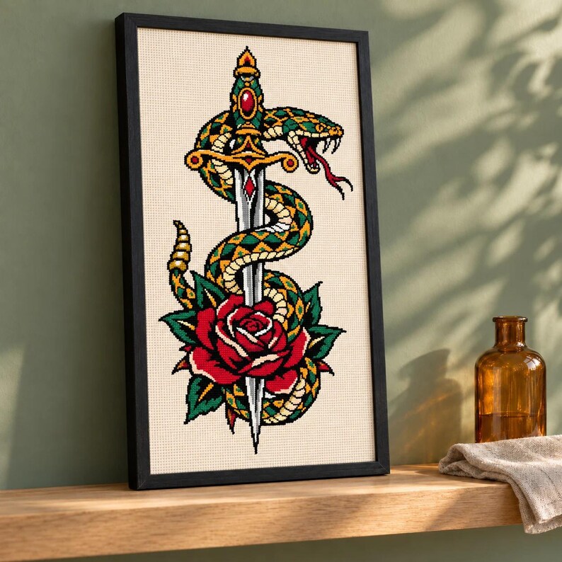 Tall snake and dagger cross stitch in a black frame at an angle