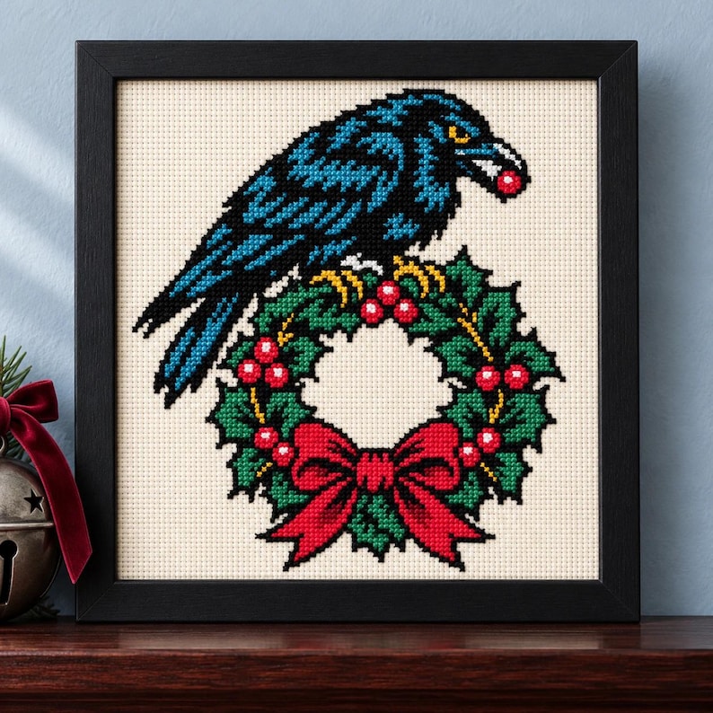 Straight-on view of the finished Raven Christmas Wreath Cross Stitch in a black frame on a wooden shelf