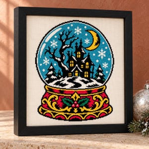 Haunted snow globe cross stitch in a tall black frame on a shelf