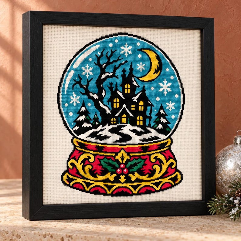 Haunted snow globe cross stitch in a tall black frame on a shelf