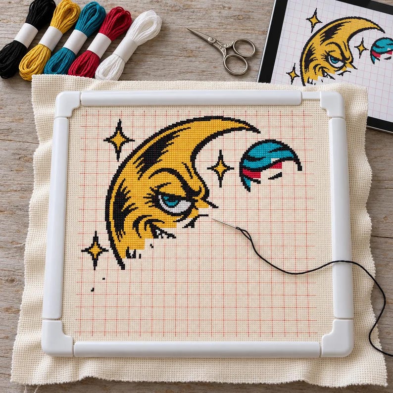 Moon cross stitch in progress in a Q-snap frame with floss, scissors and a tablet chart