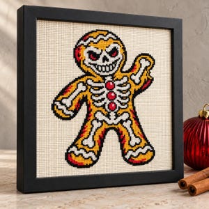 Gingerbread skeleton cross stitch in a black frame on a shelf