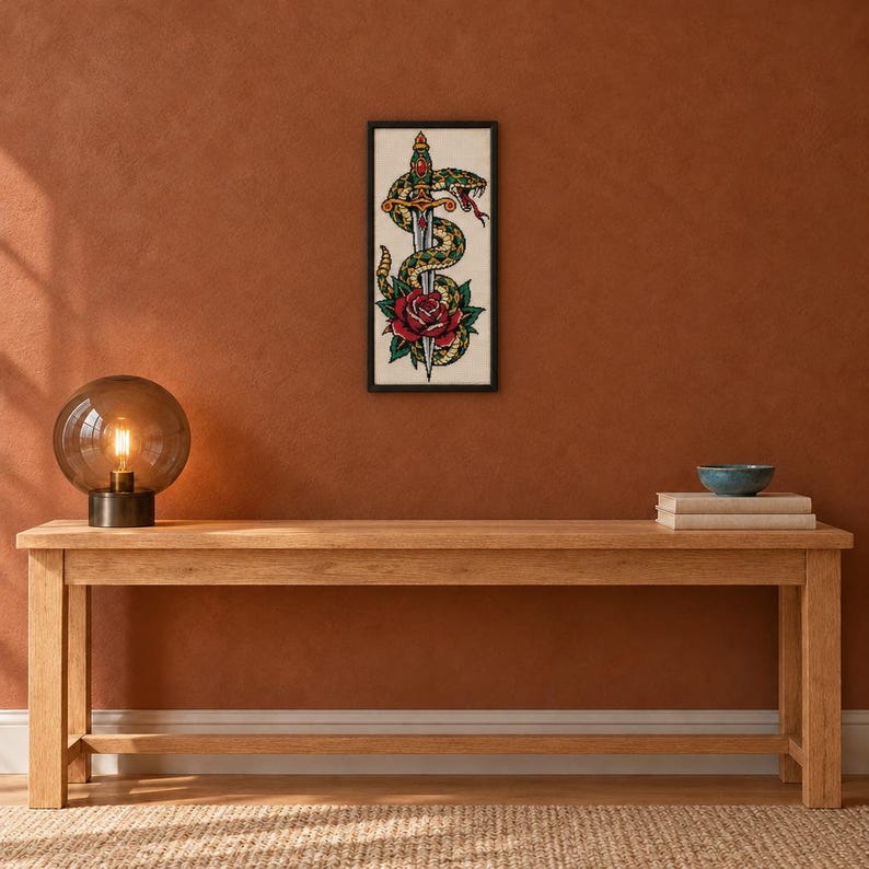 May include: A framed vertical wall art print featuring a detailed illustration of a green and yellow snake coiled around a silver dagger, positioned above a single red rose with green leaves, all set against a cream-colored background.