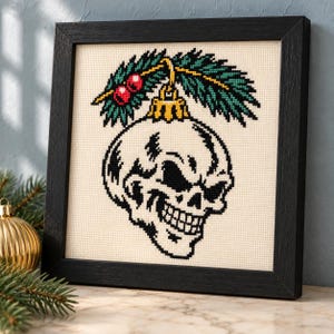 Skull ornament cross stitch in a black frame on a shelf