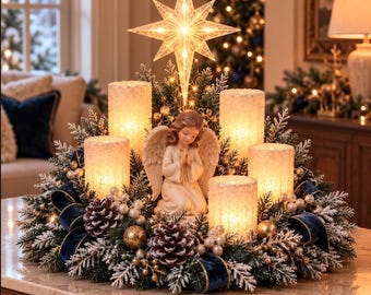 Puede incluir: Un centro de mesa navideño con una figura de ángel arrodillado rodeada por cinco velas de pilar texturizadas e iluminadas, una estrella brillante, ramas de pino escarchadas, cintas de terciopelo azul oscuro, piñas y adornos dorados.