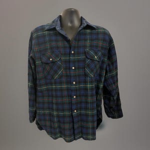 May include: A long-sleeve button-down shirt featuring a dark blue, black, and green plaid pattern with thin red and yellow accent lines. The shirt includes a standard collar, a front button placket, and two chest pockets with buttoned flaps.