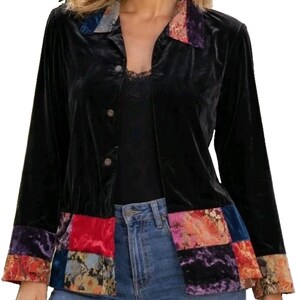 May include: A black velvet button-down shirt featuring a collar and cuffs with a multi-colored floral patchwork pattern. The hem also displays a matching patchwork design in shades of red, blue, purple, and orange, contrasting with the solid black body.