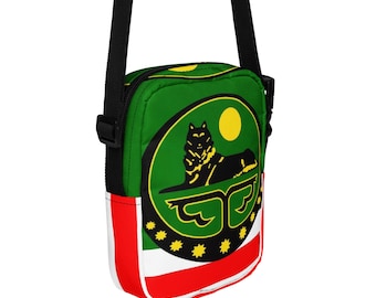 May include: A rectangular crossbody bag featuring a green, white, and red horizontal striped pattern. The front displays a circular emblem with a black wolf silhouette, a yellow sun, and a row of nine yellow stars along the bottom edge.
