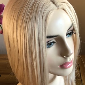 Peut inclure: T&ecirc;te de mannequin avec une perruque blonde. La perruque pr&eacute;sente des cheveux raides, mi-longs, avec une raie naturelle. Le mannequin a les yeux bleus et les l&egrave;vres roses, sur fond neutre.
