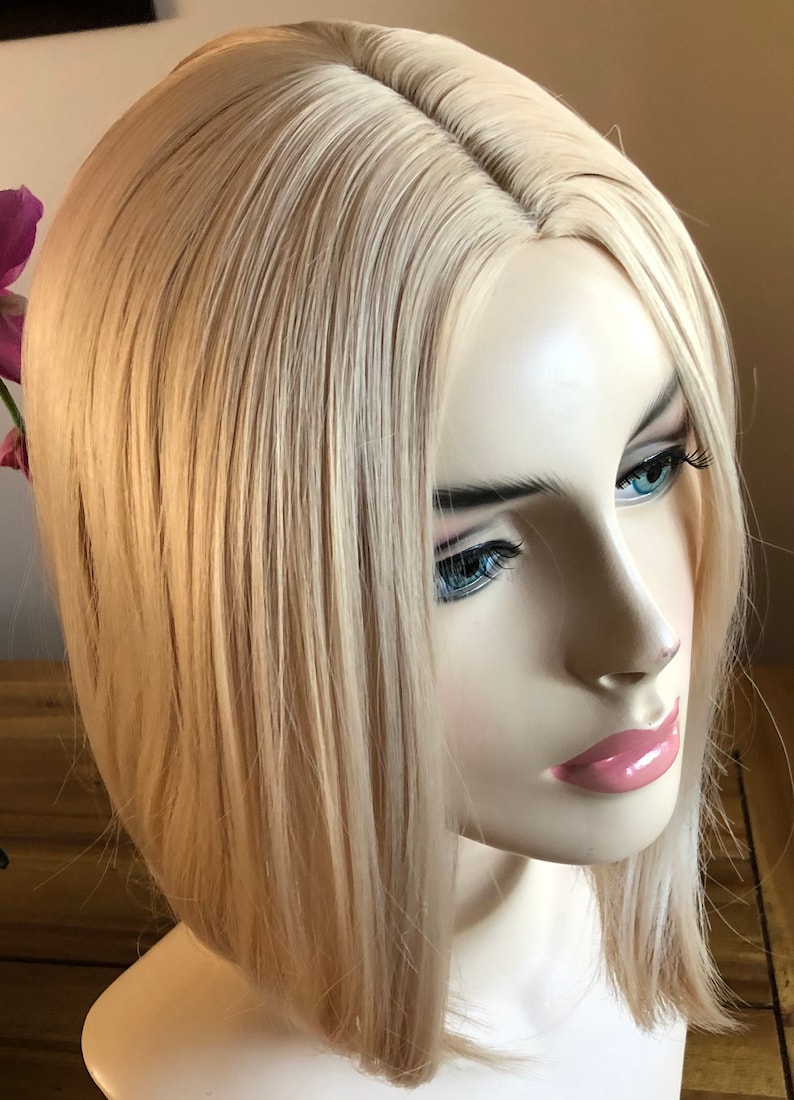 Peut inclure: T&ecirc;te de mannequin avec une perruque blonde. La perruque pr&eacute;sente des cheveux raides, mi-longs, avec une raie naturelle. Le mannequin a les yeux bleus et les l&egrave;vres roses, sur fond neutre.