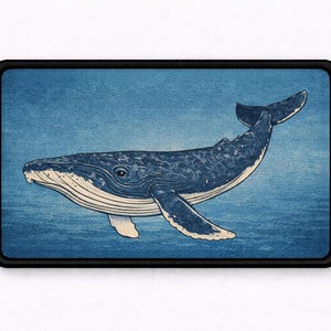 May include: A rectangular patch featuring a detailed illustration of a humpback whale swimming in deep blue water. The whale is rendered in shades of dark blue and white with a textured appearance, framed by a solid black border.