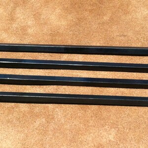 以下が含まれることがあります： 装飾的なループハンドルが付いた、黒い金属製の串が4本。串は長く細く、先端は尖っています。ハンドルは渦巻き模様の装飾的なデザインです。串は茶色の表面に配置されています。