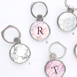 May include: Five different marble phone ring holders. Each ring holder has a different marble pattern and a letter on the front. The letters are R and T. The ring holders are numbered 1 through 5.