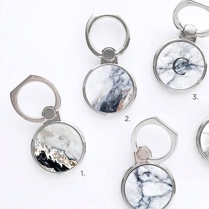 May include: Five different marble phone ring holders with silver metal rings. The marble designs are white and gray with black veins. The rings are numbered 1 through 5.