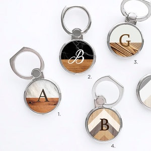 May include: Wood print finger rings/stands with silver ring holders. The rings feature various wood grain and marble designs, with letters A, B, G, and F. The text "Wood Print Finger Rings/Stands" is at the top.