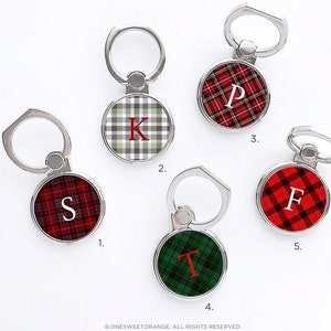 May include: Five phone ring holders with different plaid patterns and initial letters. The rings are silver and the patterns are red and green plaid, red and white plaid, and green and white plaid.