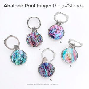 May include: Five silver phone ring holders with a circular abalone shell design. Each ring holder has a different pattern of iridescent blue, green, and pink.
