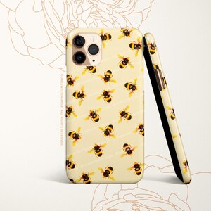May include: A cream-colored phone case with a repeating pattern of yellow and brown bees. The case is designed for an iPhone with a triple lens camera.