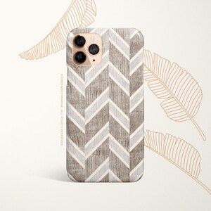 May include: A phone case with a chevron pattern in shades of gray and white. The case has a wood grain texture and is designed for a phone with a triple camera system.