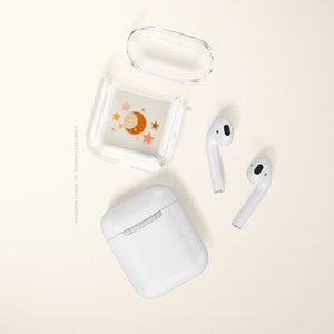 May include: A clear plastic case with a moon and stars design for wireless earbuds. The case is open and the earbuds are sitting next to it.