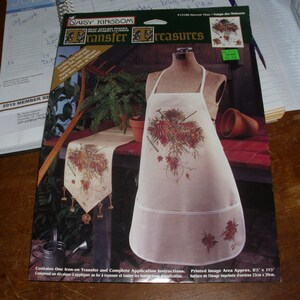 May include: A Daisy Kingdom Transfer Treasures iron-on transfer featuring a fall-themed design with a table runner and an apron. The design includes a bouquet of red and orange flowers, leaves, and vines. The printed image area is approximately 67 inches by 11 1/2 inches.