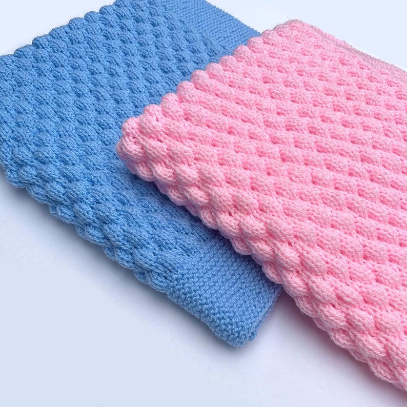 May include: Two knitted blankets, one light blue and one pink, are displayed side-by-side. The blankets have a textured, bubble-like pattern and a smooth border. The soft, cozy blankets are ideal for babies or as decorative throws.