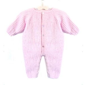 Puede incluir: Un pelele de beb&eacute; de punto rosa claro, con mangas largas y botones en la parte delantera. La prenda est&aacute; hecha de un hilo suave y texturizado y se muestra en una percha blanca. Dise&ntilde;ado para beb&eacute;s y ni&ntilde;os peque&ntilde;os.