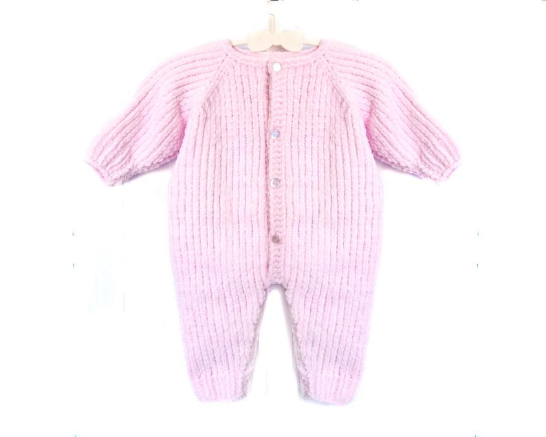 Puede incluir: Un pelele de beb&eacute; de punto rosa claro, con mangas largas y botones en la parte delantera. La prenda est&aacute; hecha de un hilo suave y texturizado y se muestra en una percha blanca. Dise&ntilde;ado para beb&eacute;s y ni&ntilde;os peque&ntilde;os.