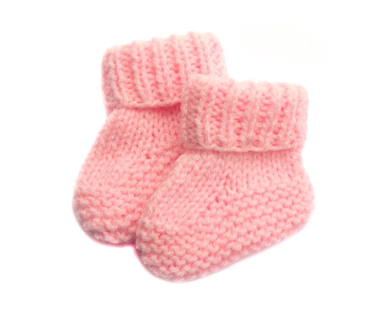 May include: A pair of pink knitted baby booties. The booties are made of a soft, fluffy yarn and have a simple, classic design.