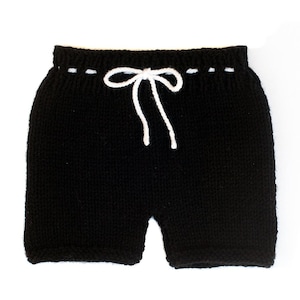 Puede incluir: Shorts negros de punto con cordón blanco. Los shorts tienen un diseño sencillo con un cordón blanco y un detalle de costura blanco en la cintura. Los shorts están hechos de un material de punto suave.