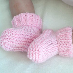 May include: A pair of pink knitted baby booties with a fold-over cuff.