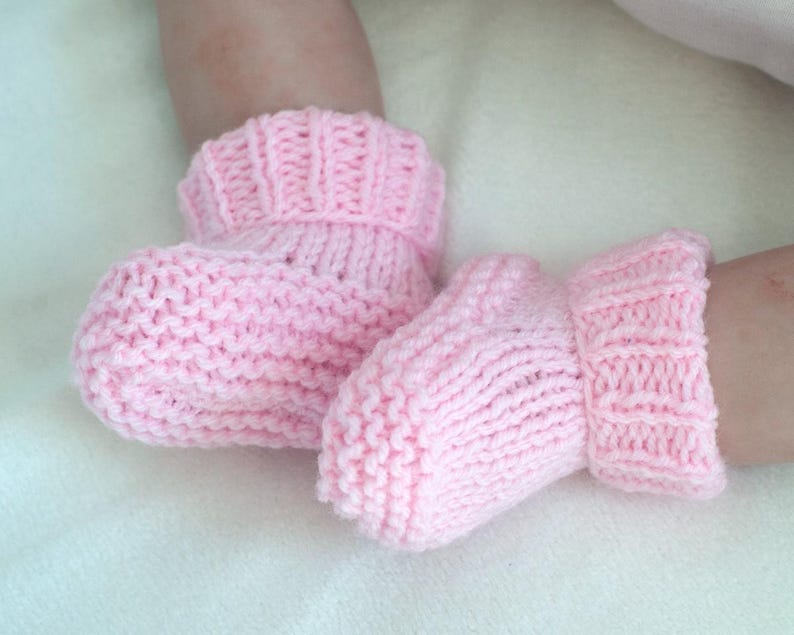 May include: A pair of pink knitted baby booties with a fold-over cuff.