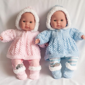 May include: Two baby dolls wearing knitted outfits. The doll on the left is wearing a pink knitted dress and hat with white trim. The doll on the right is wearing a blue knitted dress and hat with white trim.
