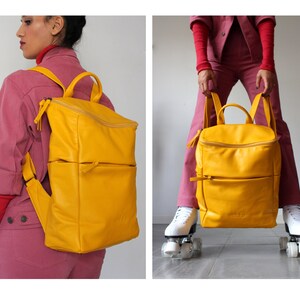 May include: A bright yellow leather backpack with two zippered compartments and a top zipper closure. The backpack is being worn by a person and also held in front of a person on roller skates.