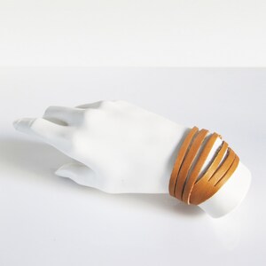 May include: A tan leather bracelet with multiple strands wrapped around a wrist.