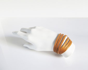 May include: A tan leather bracelet with multiple strands wrapped around a wrist.