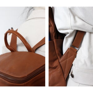May include: A brown leather backpack with adjustable straps. The backpack has a zippered closure and a top handle.