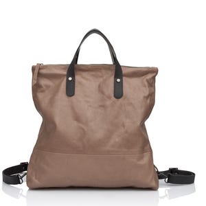Puede incluir: Un bolso tote de cuero marr&oacute;n con asas y correas de cuero negro. El bolso tiene una cremallera y una solapa con cierre magn&eacute;tico.