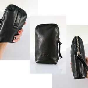 Könnte beinhalten: Schwarze Leder-Reißverschlusstasche mit goldenem Reißverschluss und einem kleinen Leder-Quaste. Die Tasche hat die Initialen "JJD" auf der Vorderseite geprägt.