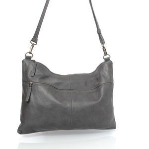May include: A gray leather shoulder bag with a long strap and a zipper closure. The bag has a flap with a zippered pocket on the front.