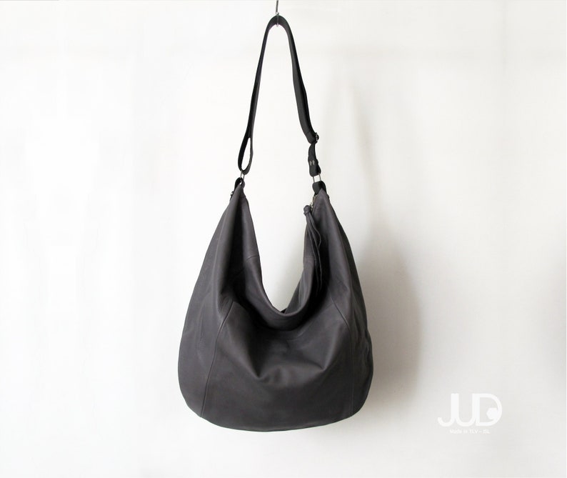May include: A large, dark grey leather tote bag with a long shoulder strap. The bag has a slouchy, casual look and is hanging from a hook.