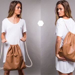 May include: Two women wearing white t-shirts with a brown leather drawstring bag. The bag has a white drawstring and is worn over the shoulder.