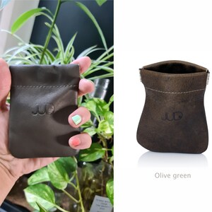 May include: A small, olive green leather pouch with a drawstring closure and a stitched design. The pouch has the initials "JD" embossed on the front.