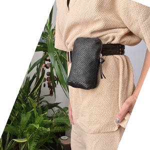May include: A black woven leather fanny pack with a brown leather belt. The fanny pack is worn over a beige knitted top.