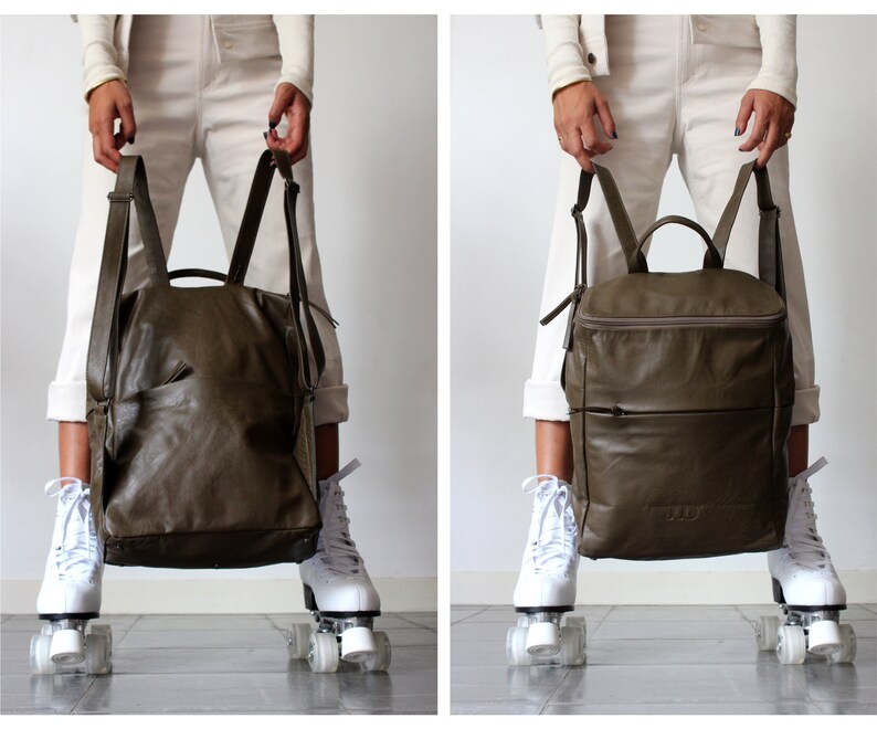 May include: A dark green leather backpack with a zippered pocket on the front. The backpack is being held by a person wearing white pants and white roller skates.