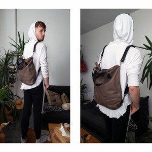 May include: A brown leather convertible backpack with black straps and a zipper closure. The backpack is being worn by a person wearing a white hoodie and black pants.