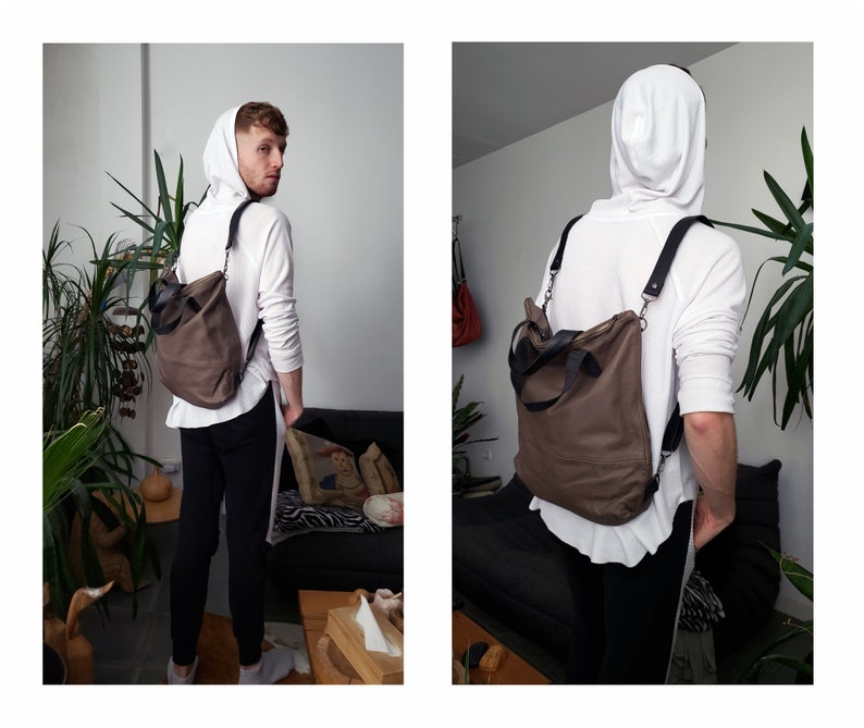 May include: A brown leather convertible backpack with black straps and a zipper closure. The backpack is being worn by a person wearing a white hoodie and black pants.