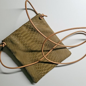 Könnte beinhalten: Eine kleine, olivgrüne Ledertasche mit Schlangenleder-Optik und einem braunen Lederriemen. Die Tasche hat einen Kordelverschluss.