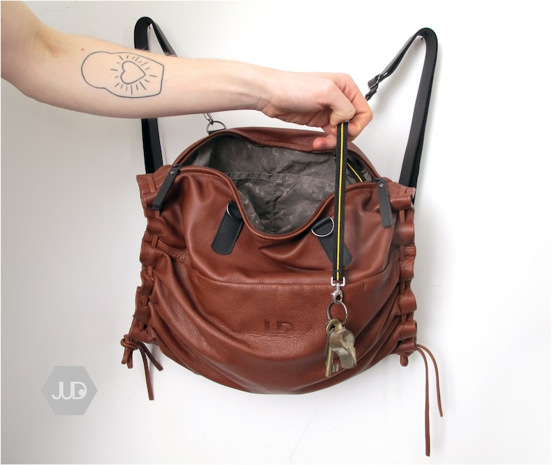 May include: A brown leather backpack with a yellow and black strap. The bag is open and has a key chain attached to the inside.